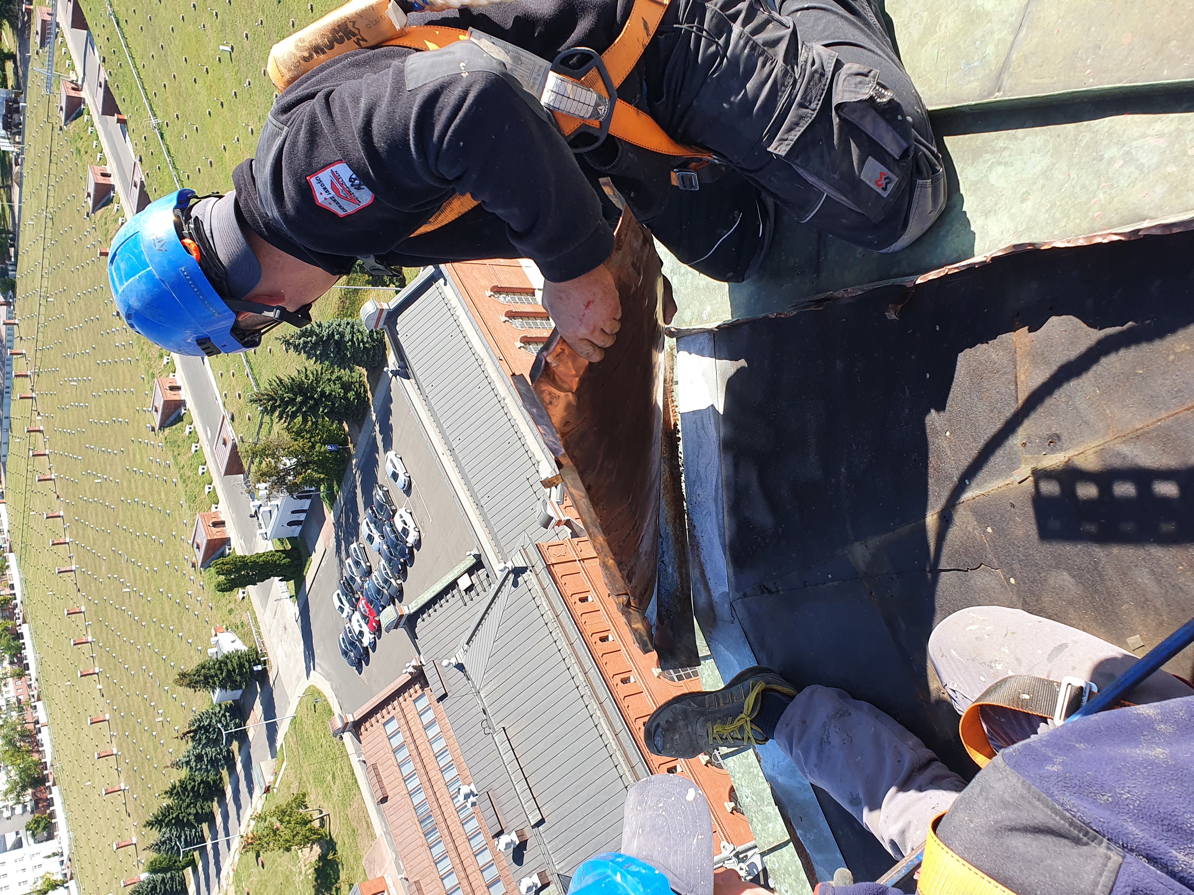 pracownicy w uprzężach na dachu wieży ciśnień, w tle zabudowania Stacji Filtrów