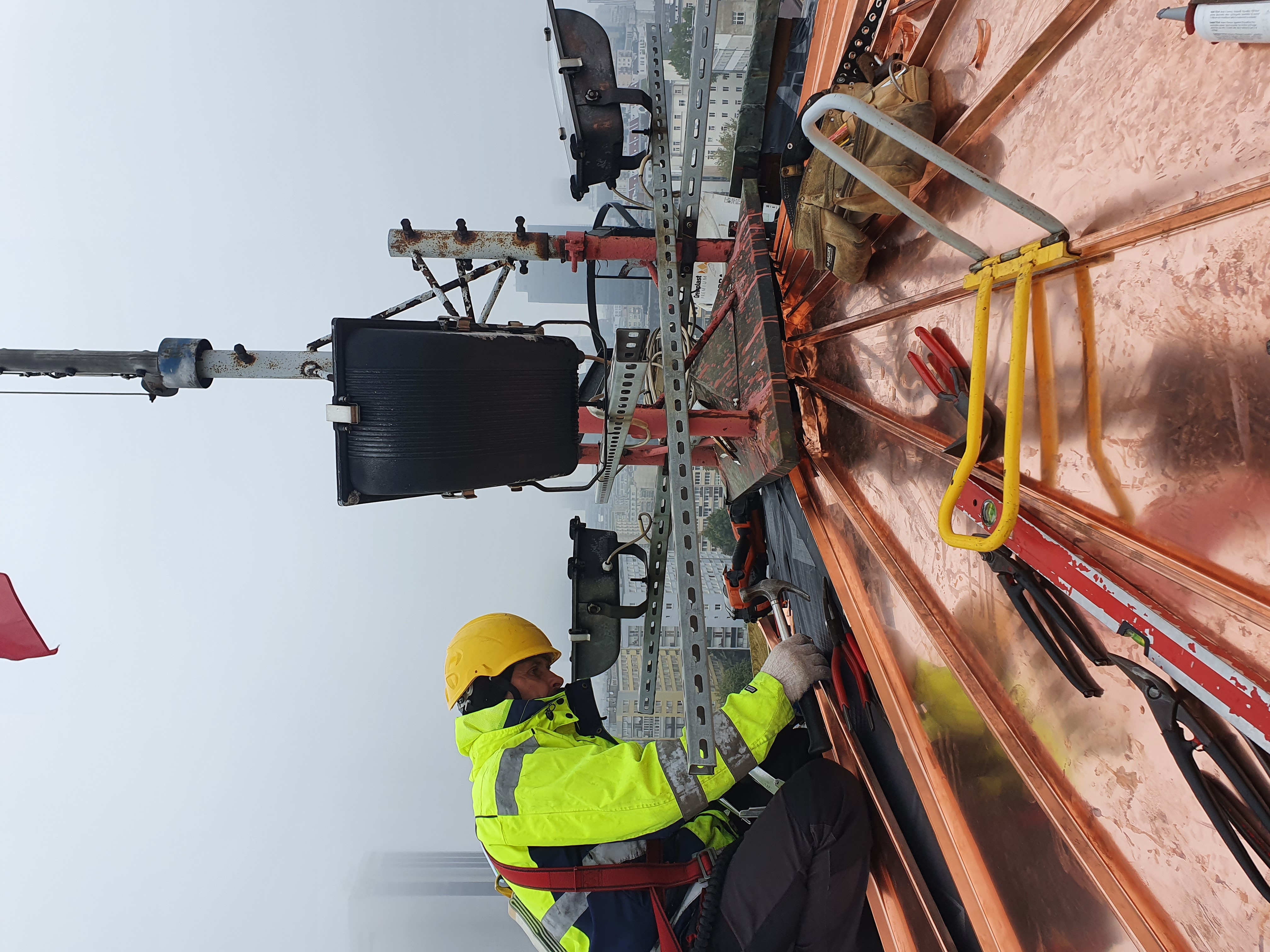 pracownik na szczycie wieży ciśnień montujacy nowe elementy pokrycia dachu 